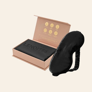 Pillowcase and Sleep Mask in Mulberry Silk by Lenoites featuring a black silk sleep mask and a black mulberry silk pillowcase presented in an open blush pink box against a soft light background.